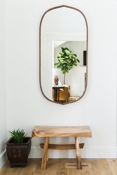 a wooden bench sitting in front of a mirror on the wall next to a potted plant