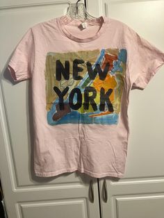 a pink shirt with the words new york on it hanging from a hook in front of a white door