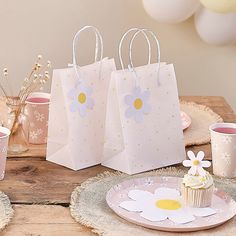 three paper bags with flowers on them sitting on a table next to cupcakes