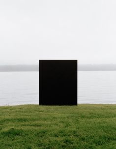 a black square sitting on top of a lush green field next to the ocean in front of a body of water