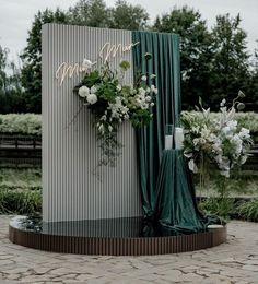 an outdoor ceremony setup with flowers and greenery on the side, surrounded by green drapes