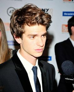 a young man in a suit and tie talking to the camera while holding a microphone