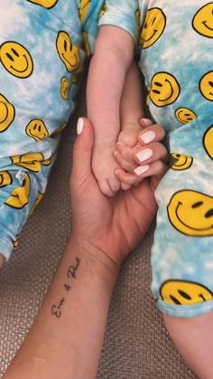 two people holding hands with smiley faces on their sleeves and wrist tattoos, both wearing matching pajamas