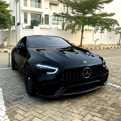 a black sports car parked in front of a white building on a brick road next to trees