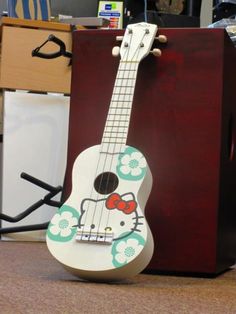 an ukulele is sitting on the floor in front of a wooden box with a hello kitty design