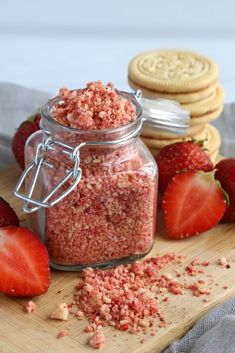 a jar filled with pink sugar next to strawberries and cookies on a cutting board