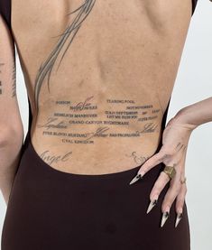 the back of a woman with tattoos on her upper and lower body, showing words written in cursive writing