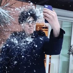 a man taking a selfie in the snow with his cell phone while it's snowing