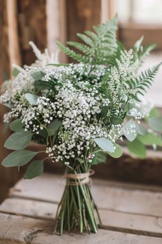 a vase filled with lots of white flowers and greenery on top of a wooden table