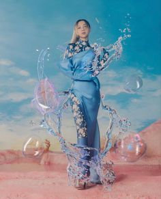 a woman in a blue dress with bubbles floating around her and the sky behind her