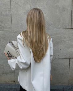 a woman with long blonde hair is holding a white purse and looking at the wall