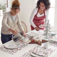 two women in aprons are decorating a table with plates, cups and silverware