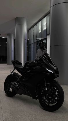 a person sitting on a black motorcycle in front of a building with columns and windows