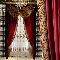 a room with red curtains and gold trimmings on the walls, windows, and chandelier