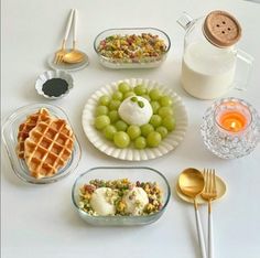 a white table topped with plates and bowls filled with food next to a jug of milk