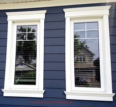 two windows on the side of a blue house with white trim and shutters are shown