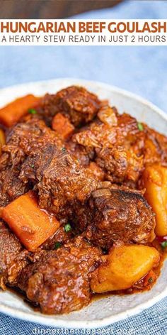 beef goulash with carrots and potatoes in a white bowl on a blue table cloth