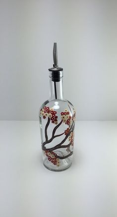 a glass bottle with a silver top and red flowers painted on the bottom, sitting on a white surface