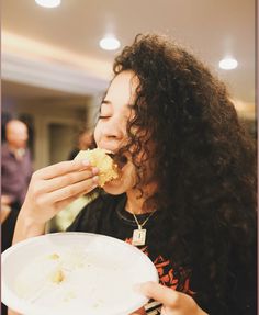 a woman with curly hair eating food from a white bowl on top of a table