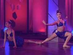 two women are dancing on the stage in blue outfits and one is wearing a headband