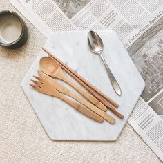 wooden utensils and spoons are on a marble tray next to a newspaper