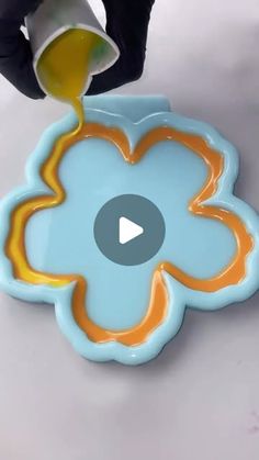 someone is pouring orange liquid on a flower shaped plate with yellow and blue designs in the center