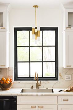 a kitchen with white cabinets, black windows and a bowl of oranges on the counter