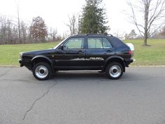 a black suv parked on the street in front of some grass and trees with no leaves