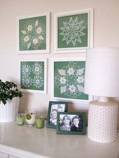 three green and white pictures on the wall next to a lamp, vase with flowers