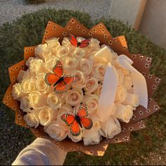 a bouquet of white roses with orange butterflies on them is held by someone's hand