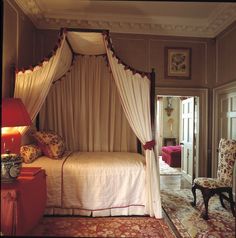 a canopy bed sitting in the middle of a bedroom next to a chair and table