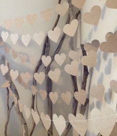 paper hearts are hanging from the branches in front of a wall with tree branches on it