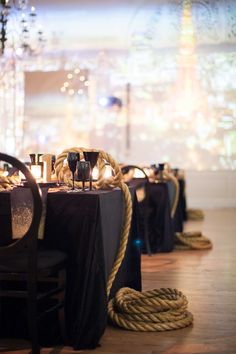 the table is set with black linens, rope and candle holders on top of it