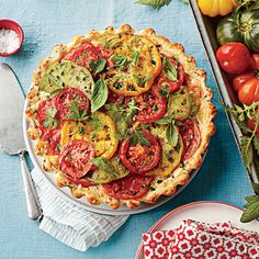 a tomato and basil quiche on a blue tablecloth next to silverware, glasses and tomatoes