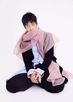 a young man sitting on the ground wearing a pink scarf over his face and black pants