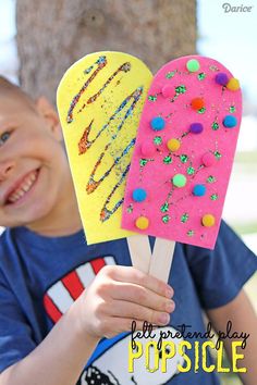 a young boy holding two popsicles covered in sprinkles and colored frosting