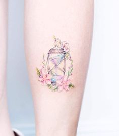 a tattoo on the leg of a woman with flowers and an hourglass in it