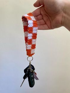 a hand holding an orange and white crocheted keychain with two keys attached to it