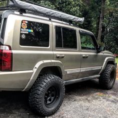 a silver jeep parked on top of a parking lot next to some trees and bushes