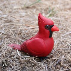 a red plastic bird sitting on top of dry grass and straw in the sun with eyes wide open