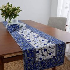 a blue and white table runner on top of a wooden dining room table with a vase of flowers