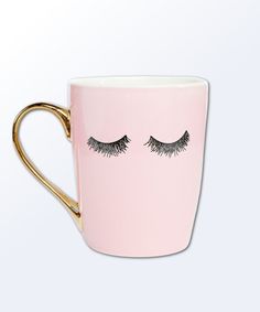 a pink coffee cup with eyelashes painted on the side and gold rimmed mug handle