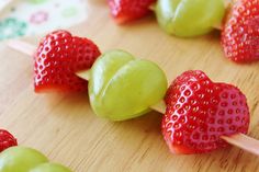 some green and red strawberries are on a wooden board with toothpicks in the shape of hearts