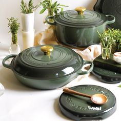 green pots and pans are sitting on a white tablecloth with herbs in them