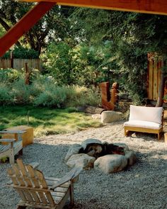 a fire pit in the middle of a gravel area with chairs and benches around it