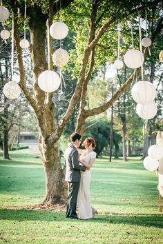 a couple standing under a tree with paper lanterns hanging from it