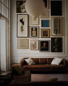 a living room filled with lots of framed pictures on the wall above a brown couch