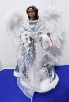 an angel statue with white wings holding a teddy bear and christmas decorations on a blue carpet