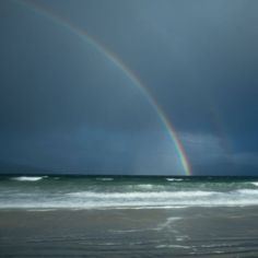 two rainbows are seen over the ocean on a cloudy day