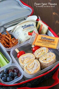 an open lunch box filled with sandwiches, fruit and veggies on a table